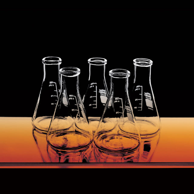 Group of scientific glass beakers on an orange table with a black background